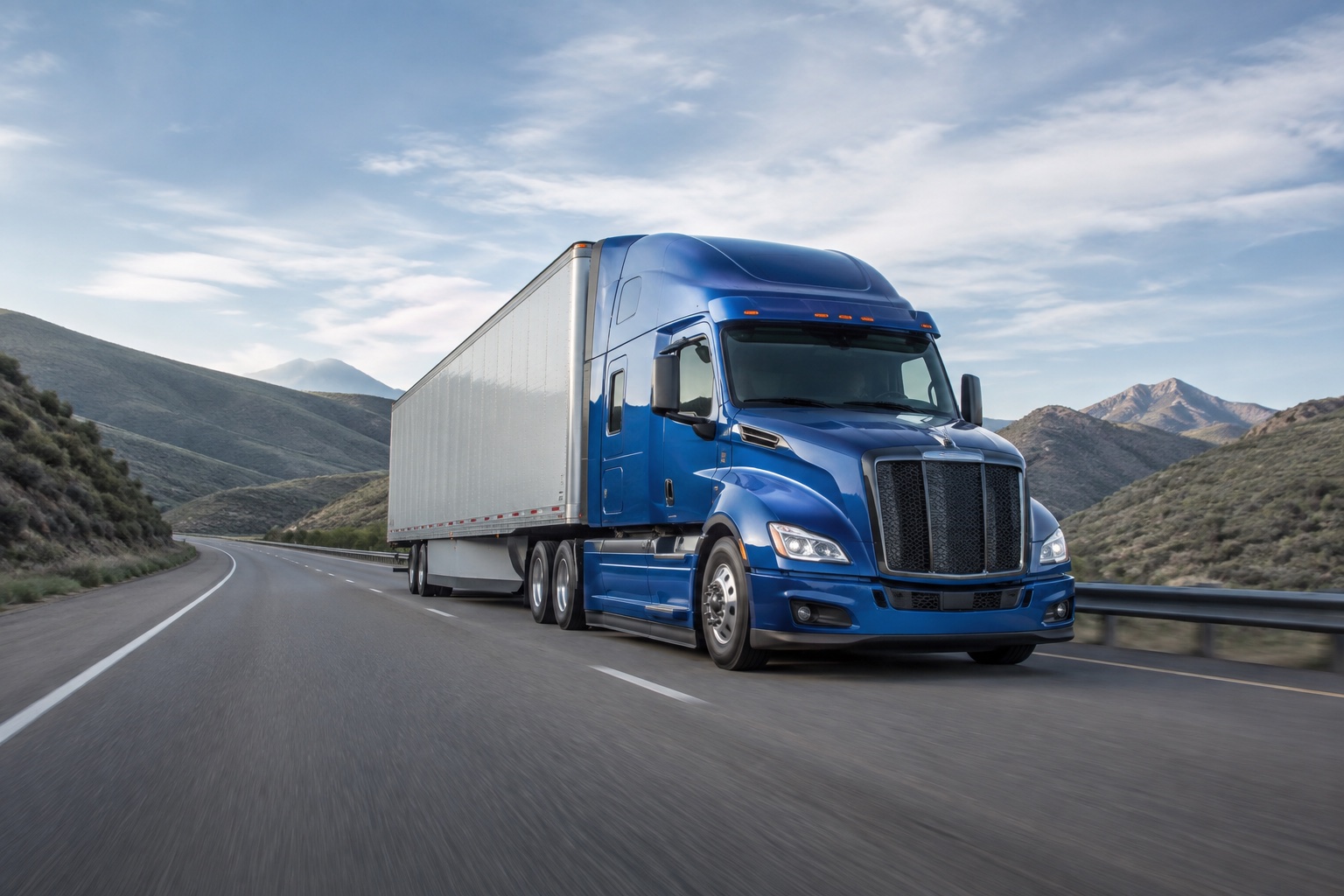 Blue semi truck travelling along an open highway through rolling hills